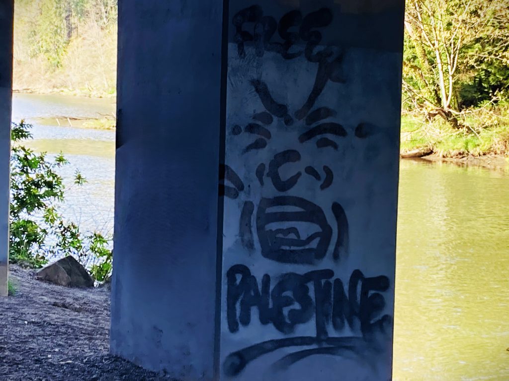 Graffiti on an electrical box, illustrated with a grimacing face and reading 'Free Palestine'