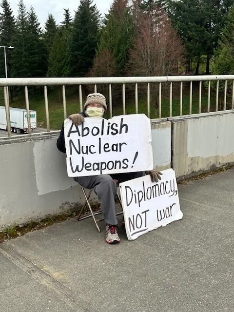 Bob Ziegler during a regular Thursday banner action over the highway, holding signs saying "Abolish Nuclear Weapons!" and "Diplomacy NOT war". Author Unknown