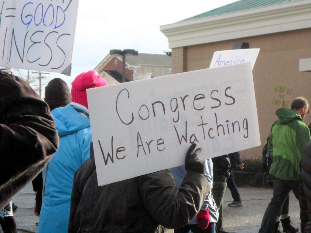 Olympia Indivisible members protesting, with one sign reading "Congress We Are Watching"